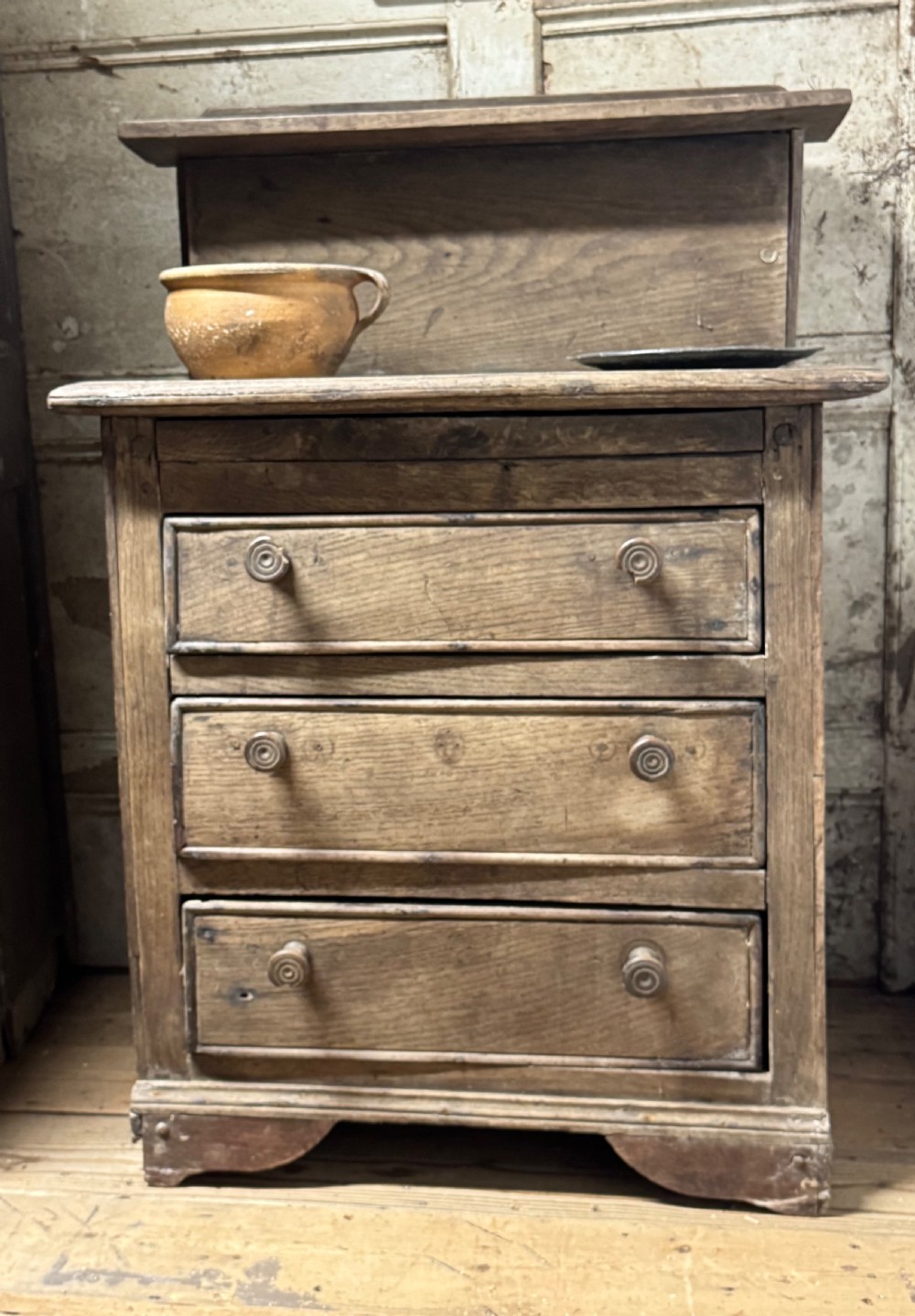 A small early 19th-century primitive oak chest featuring three drawers with turned wooden knobs and a raised wooden back shelf. View VI
