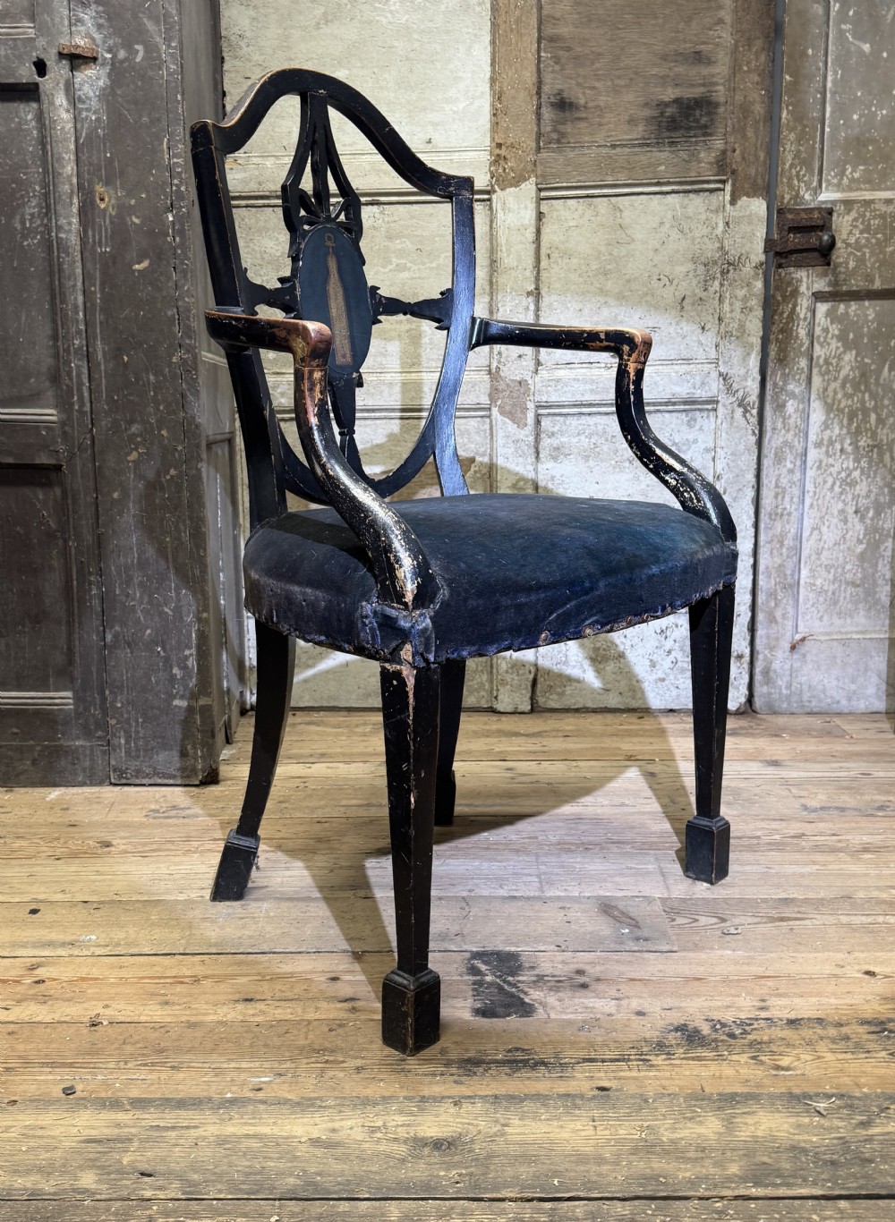 A late eighteenth-century George III black painted armchair featuring an open decorative backrest, curved arms, dark velvet upholstery, and square block feet.