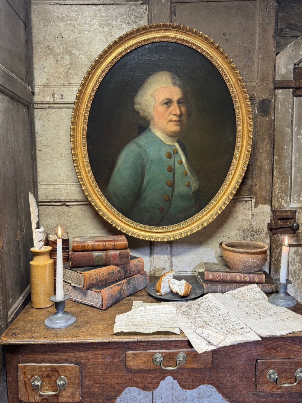 An 18th-century oval oil portrait depicting a gentleman in a blue coat and wig, set inside a carved giltwood frame.