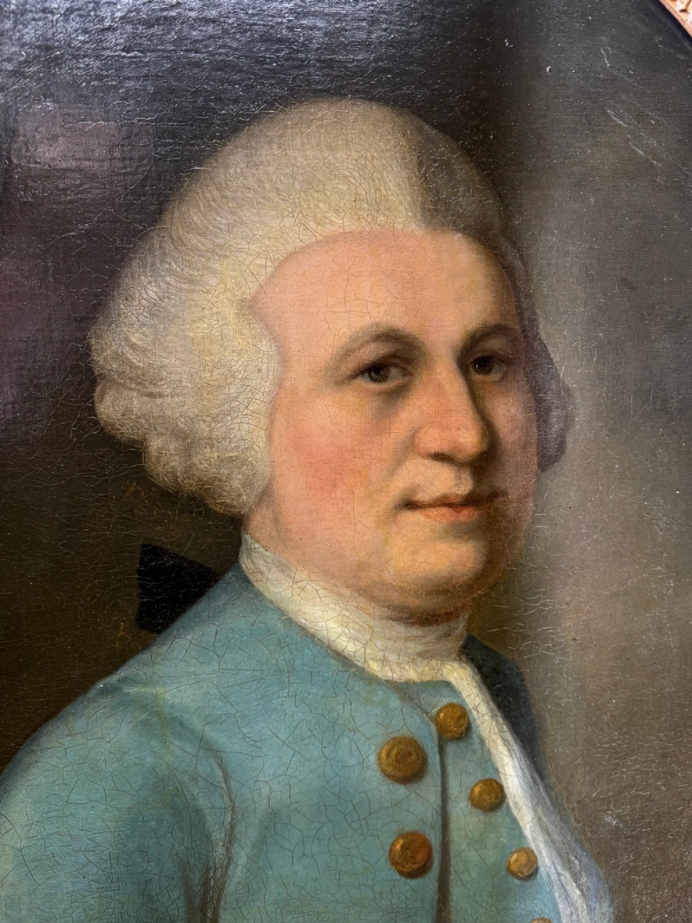An 18th-century oval oil portrait depicting a gentleman in a blue coat and wig, set inside a carved giltwood frame. View VII