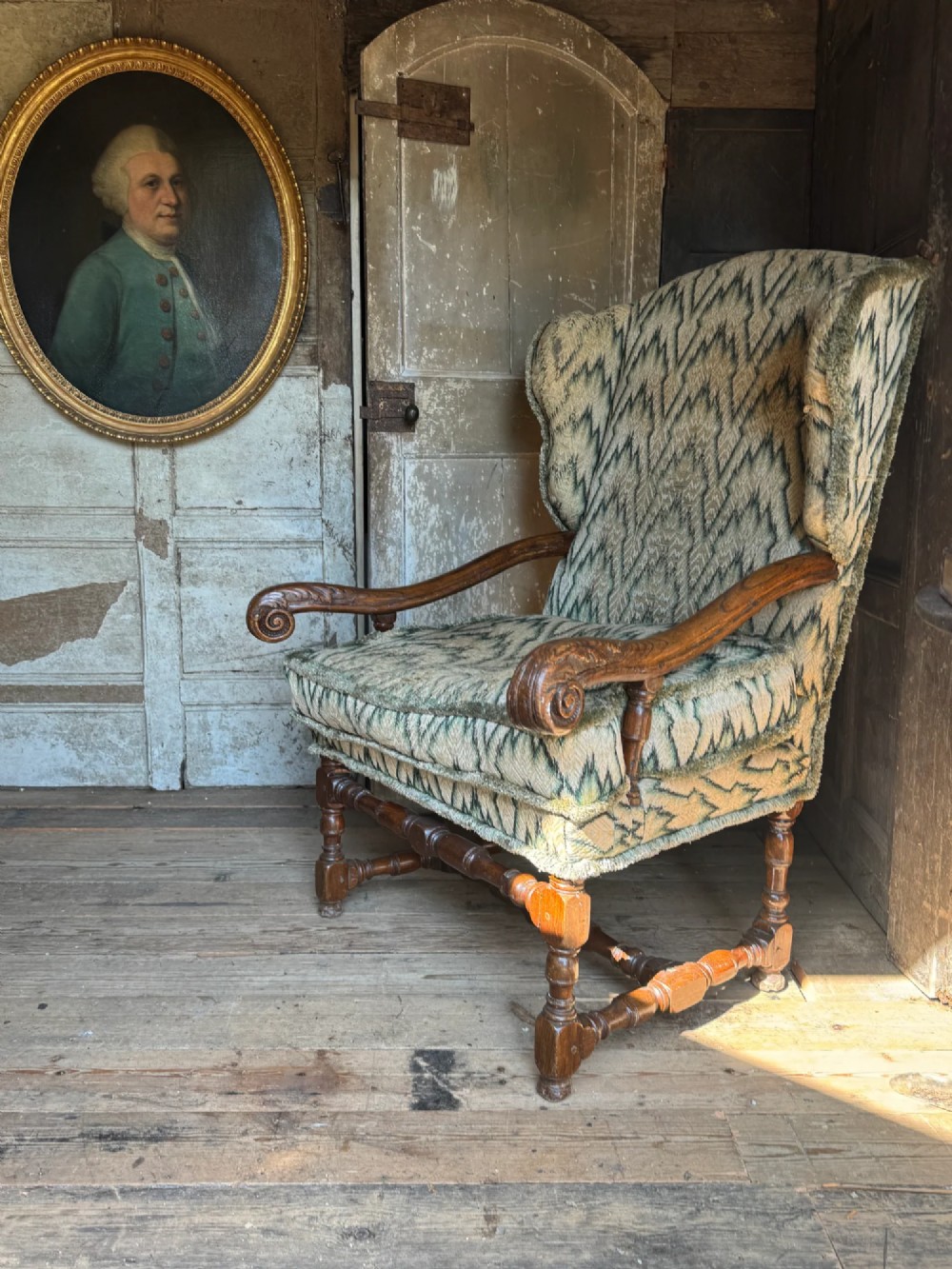 An early eighteenth-century French oak wingback armchair featuring patterned fabric upholstery, carved scroll armrests, and turned legs with stretchers. View VII