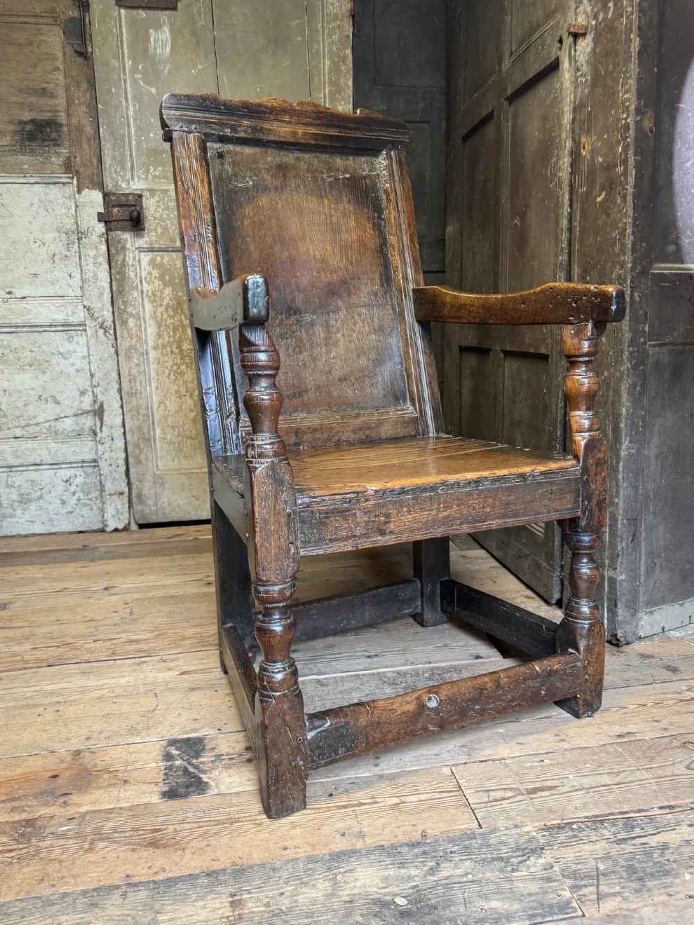 A 17th-century solid dark oak wainscot armchair featuring a panelled backrest, turned front legs, and wooden armrests. View II