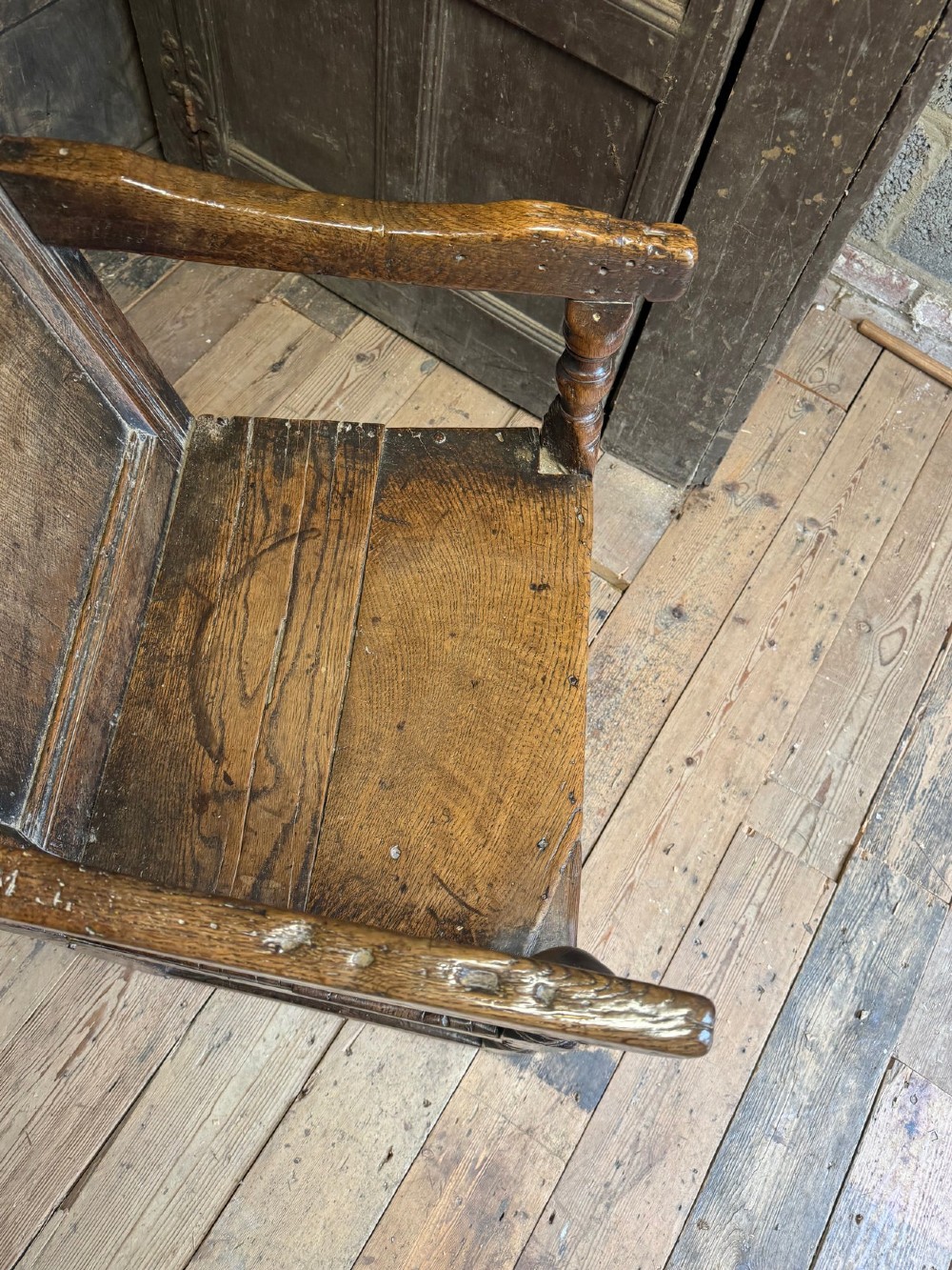 A 17th-century solid dark oak wainscot armchair featuring a panelled backrest, turned front legs, and wooden armrests. View III