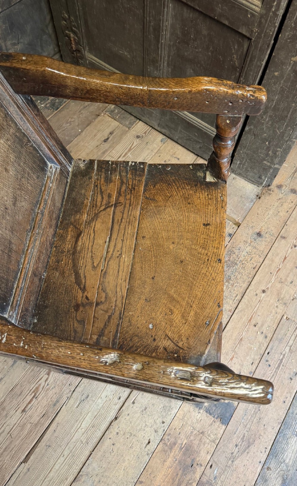 A 17th-century solid dark oak wainscot armchair featuring a panelled backrest, turned front legs, and wooden armrests. View IV