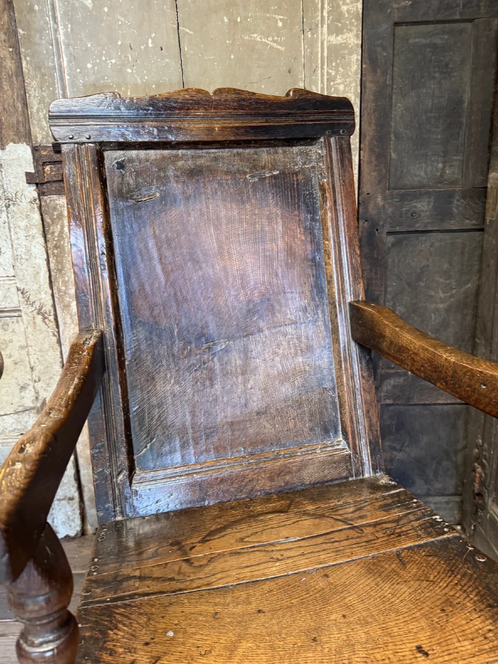 A 17th-century solid dark oak wainscot armchair featuring a panelled backrest, turned front legs, and wooden armrests. View V