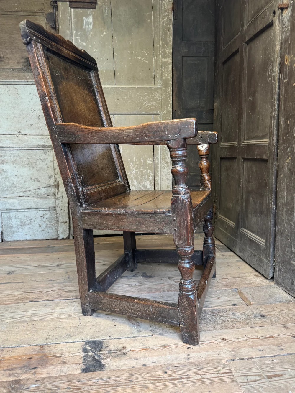 A 17th-century solid dark oak wainscot armchair featuring a panelled backrest, turned front legs, and wooden armrests. View VII
