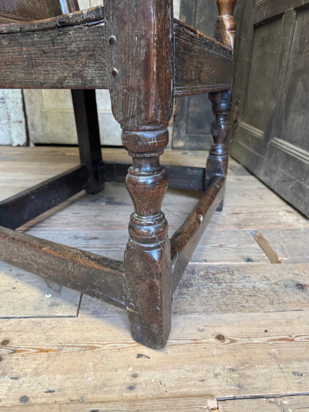 A 17th-century solid dark oak wainscot armchair featuring a panelled backrest, turned front legs, and wooden armrests. View VIII