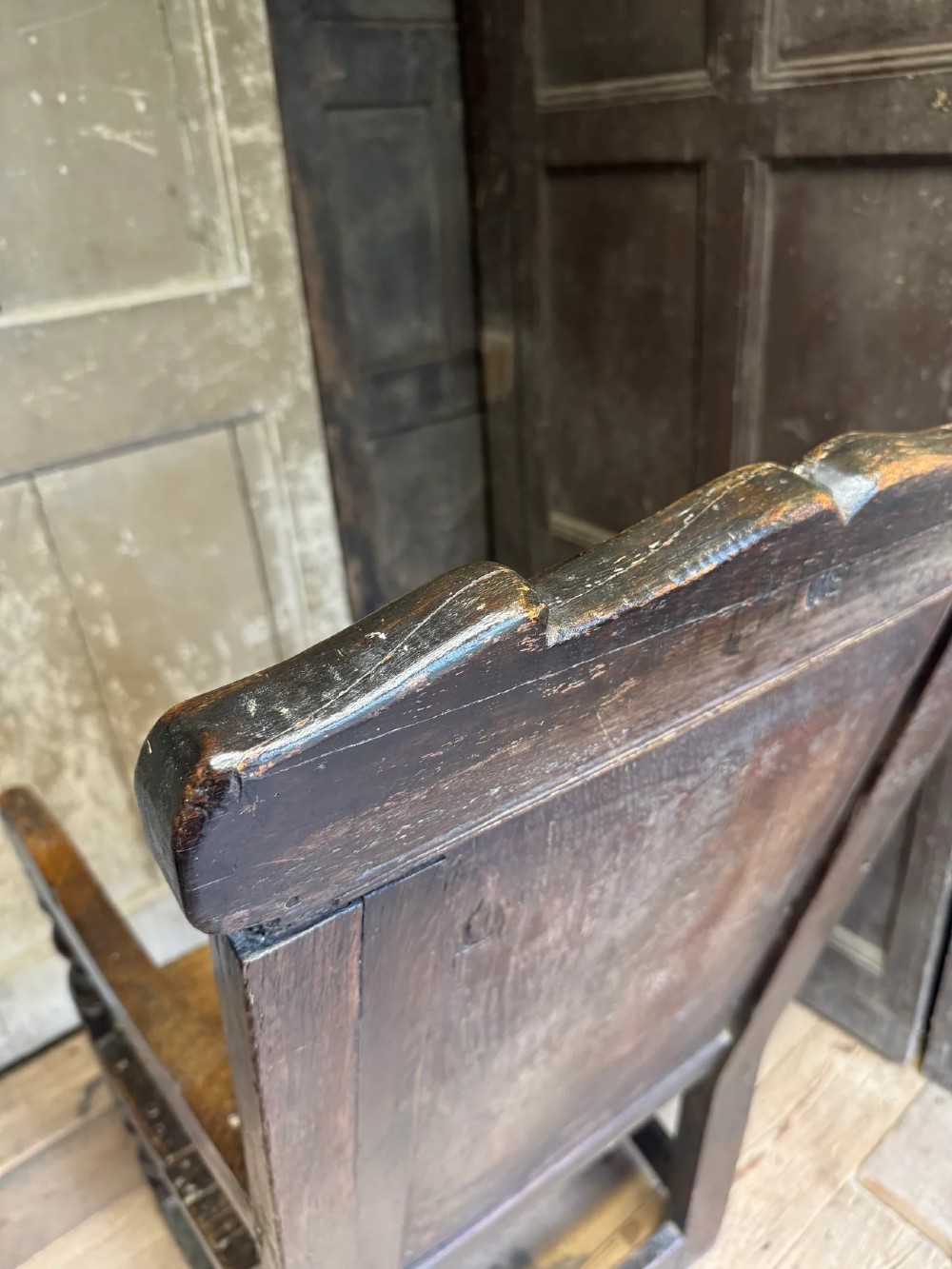 A 17th-century solid dark oak wainscot armchair featuring a panelled backrest, turned front legs, and wooden armrests. View X