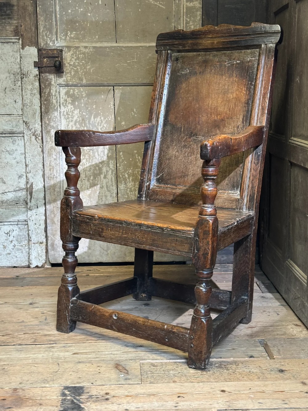 A 17th-century solid dark oak wainscot armchair featuring a panelled backrest, turned front legs, and wooden armrests. View XI