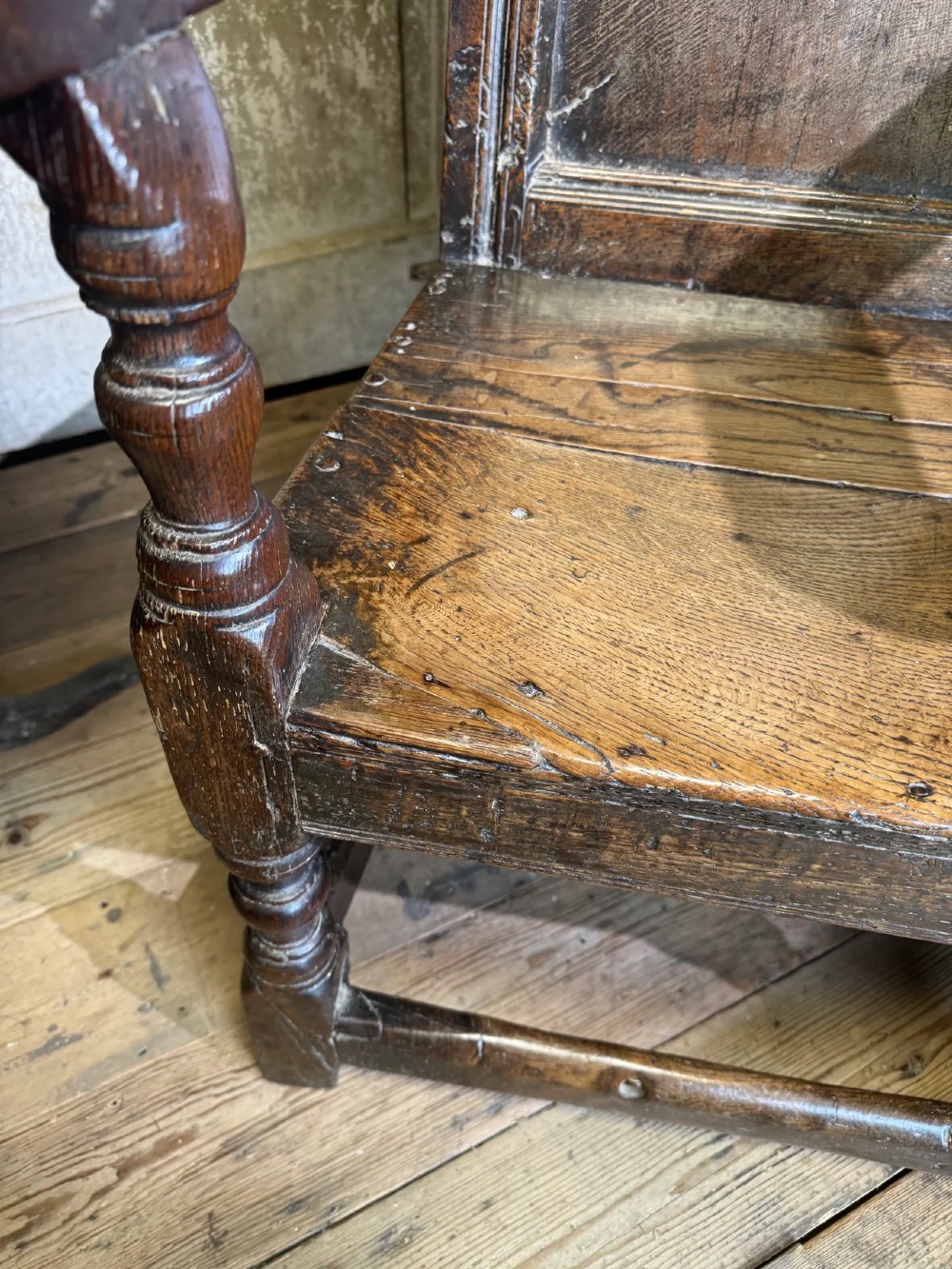 A 17th-century solid dark oak wainscot armchair featuring a panelled backrest, turned front legs, and wooden armrests. View XII