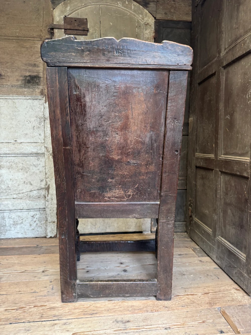 A 17th-century solid dark oak wainscot armchair featuring a panelled backrest, turned front legs, and wooden armrests. View XIII