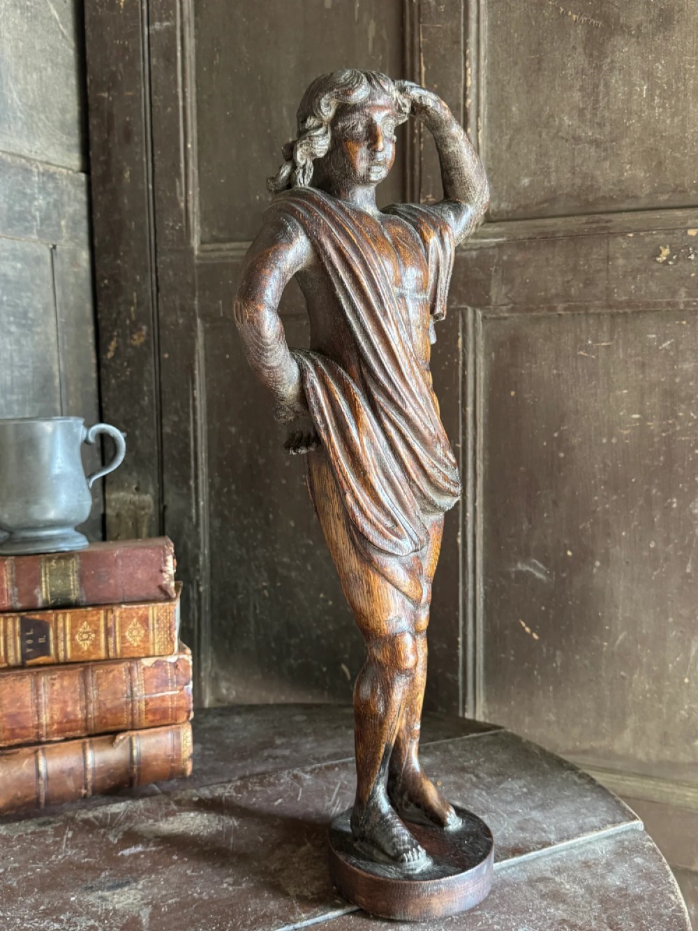 An 18th-century carved oak standing male figure with drapery across his shoulder set on a rounded base. View VII