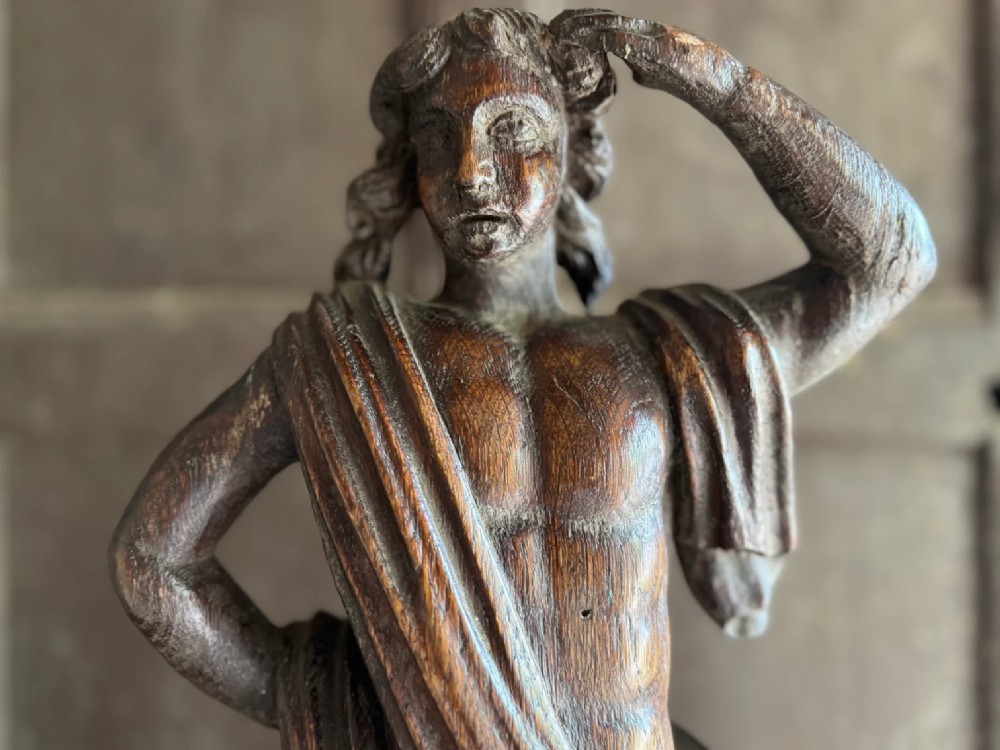 An 18th-century carved oak standing male figure with drapery across his shoulder set on a rounded base. View XIV