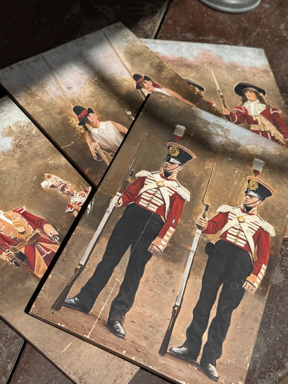 A set of four early twentieth-century wooden panels featuring hand-painted depictions of military soldiers in red uniform coats.