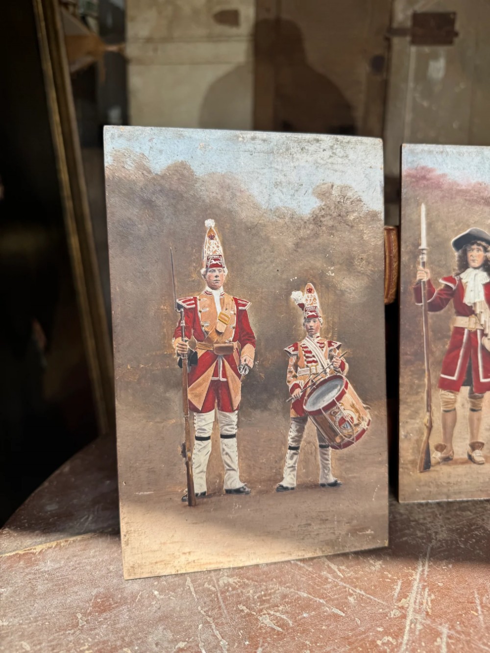 A set of four early twentieth-century wooden panels featuring hand-painted depictions of military soldiers in red uniform coats. View V