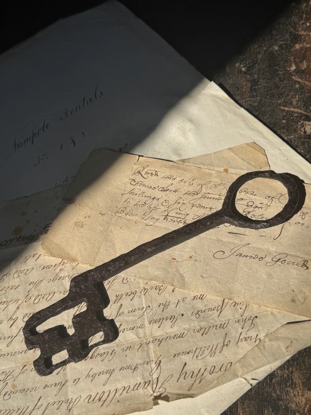 A hand-forged dark wrought iron key featuring a circular bow, a straight shaft, and a cut bit resting on manuscript paper.
