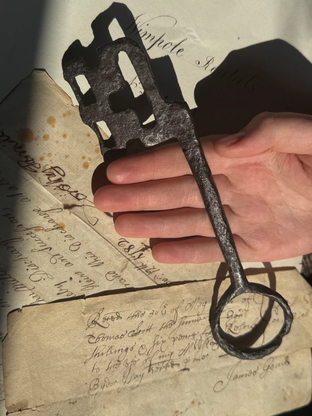 A hand-forged dark wrought iron key featuring a circular bow, a straight shaft, and a cut bit resting on manuscript paper. View II