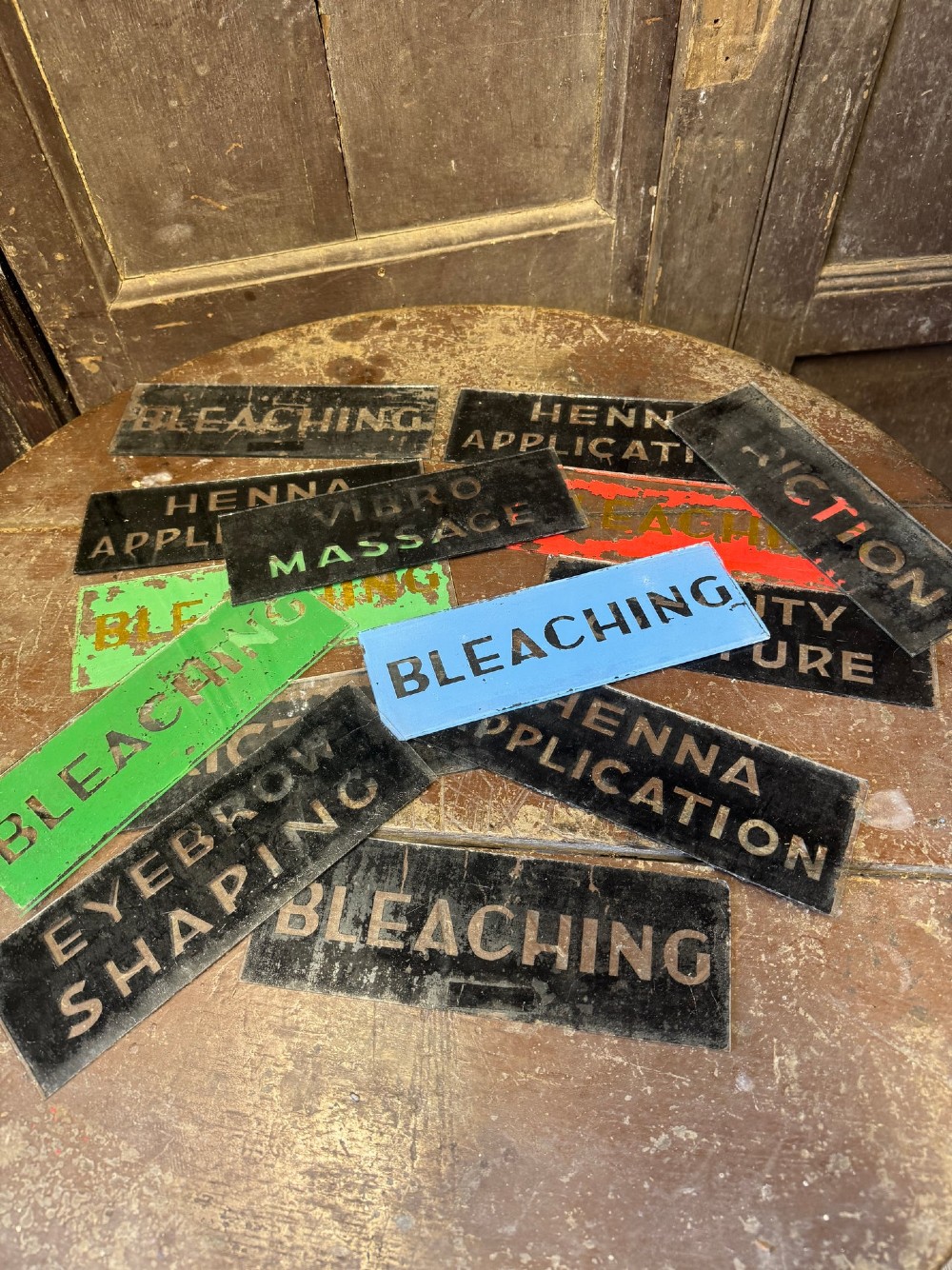 Fourteen rectangular reverse-painted glass signs detailing vintage beauty treatment terms in metallic lettering on painted backgrounds. View II