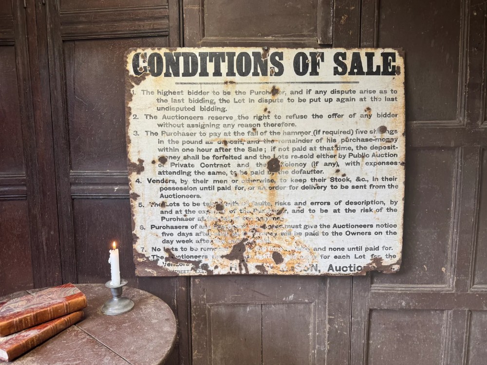 A rectangular off-white painted sheet metal sign featuring bold black typography detailing auction conditions of sale, with visible surface rust and paint wear. View II