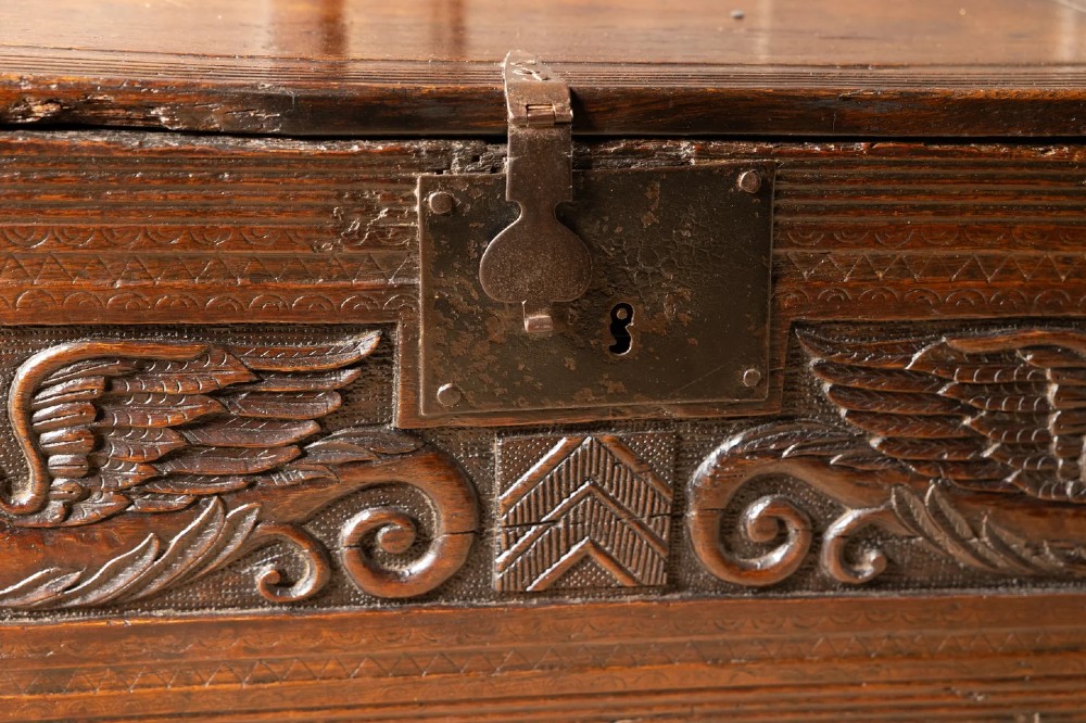 An Elizabethan carved oak boarded chest featuring relief carvings of winged mythical beasts, an iron lockplate, and slab end legs. View III