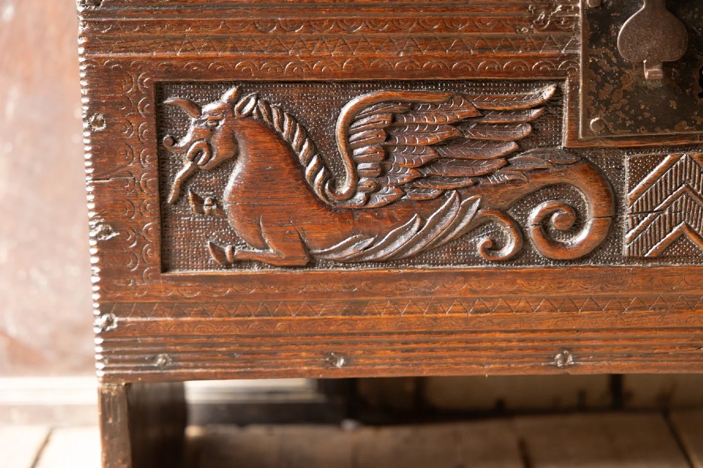 An Elizabethan carved oak boarded chest featuring relief carvings of winged mythical beasts, an iron lockplate, and slab end legs. View IV