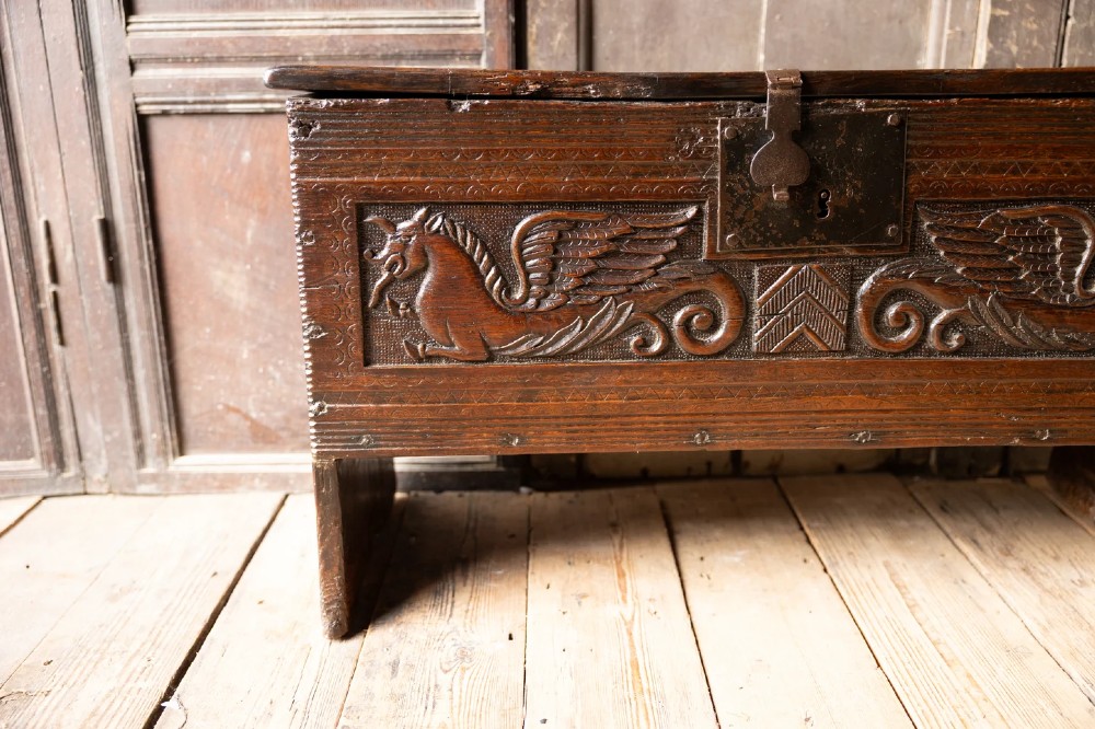 An Elizabethan carved oak boarded chest featuring relief carvings of winged mythical beasts, an iron lockplate, and slab end legs. View V