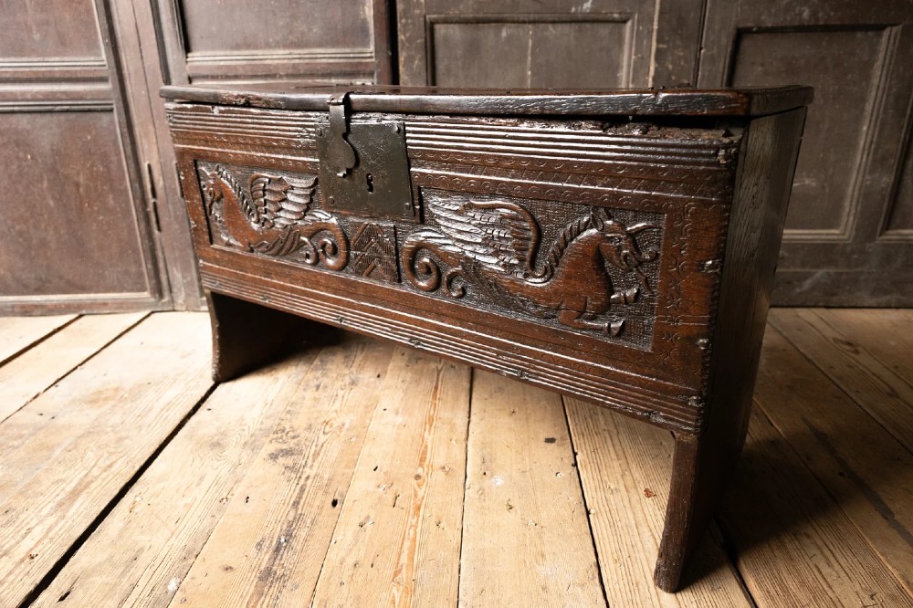 An Elizabethan carved oak boarded chest featuring relief carvings of winged mythical beasts, an iron lockplate, and slab end legs. View VIII
