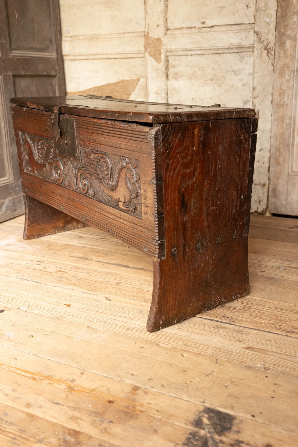 An Elizabethan carved oak boarded chest featuring relief carvings of winged mythical beasts, an iron lockplate, and slab end legs. View IX