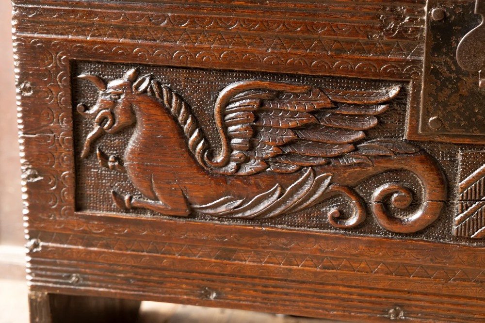 An Elizabethan carved oak boarded chest featuring relief carvings of winged mythical beasts, an iron lockplate, and slab end legs. View XIV