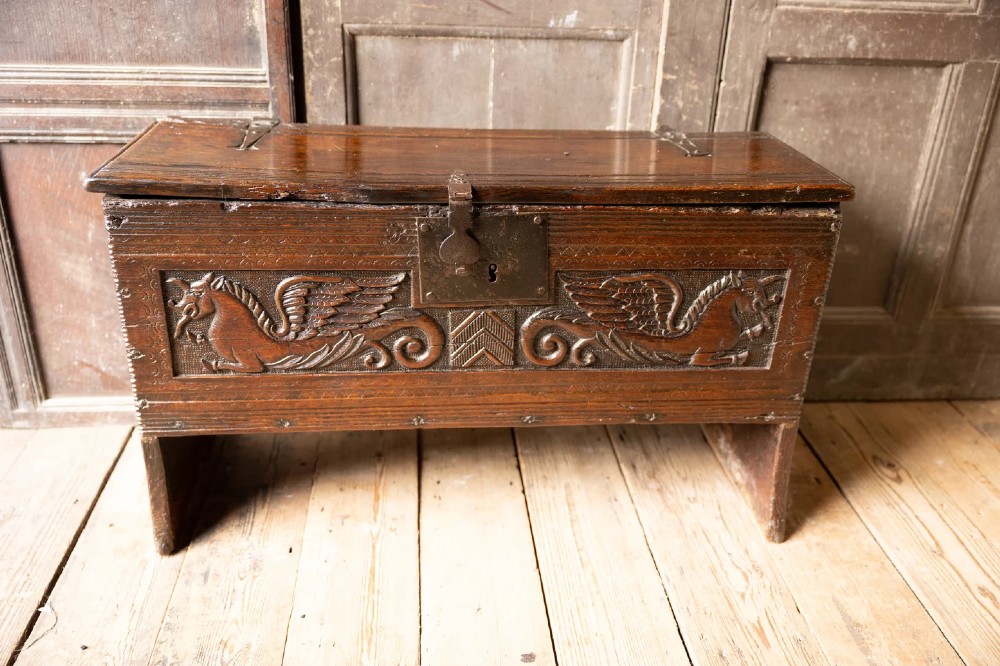 An Elizabethan carved oak boarded chest featuring relief carvings of winged mythical beasts, an iron lockplate, and slab end legs. View XV