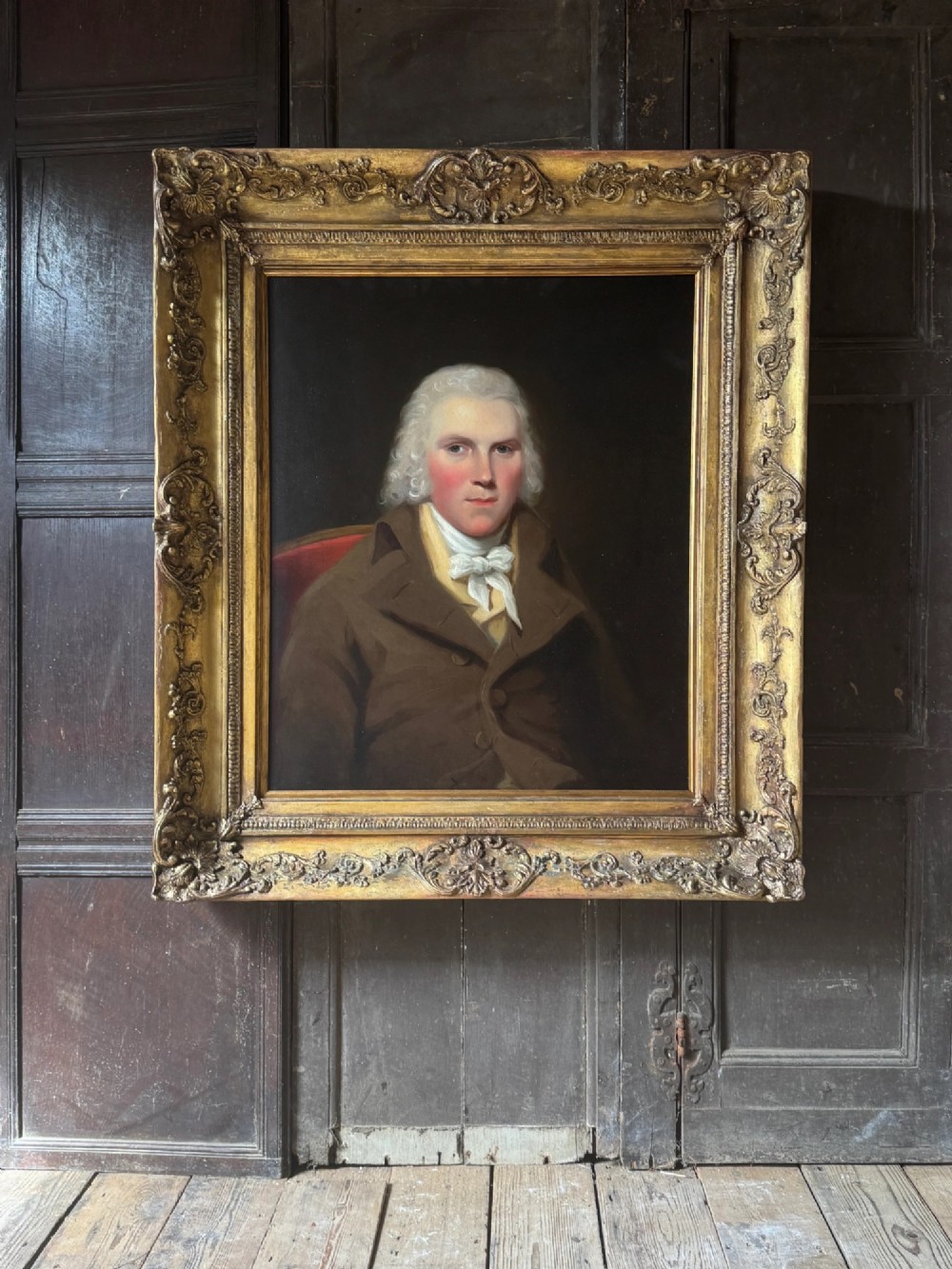 An 18th-century oil painting on canvas depicting a gentleman in a brown coat and white cravat, housed in a thick, ornate gilded frame.