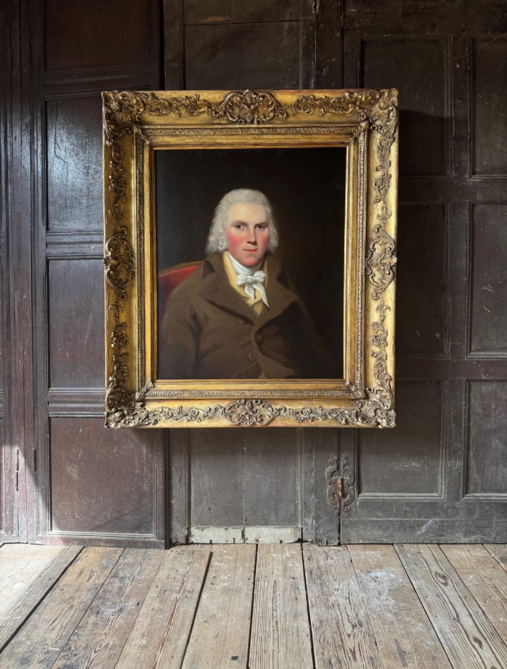An 18th-century oil painting on canvas depicting a gentleman in a brown coat and white cravat, housed in a thick, ornate gilded frame. View VIII