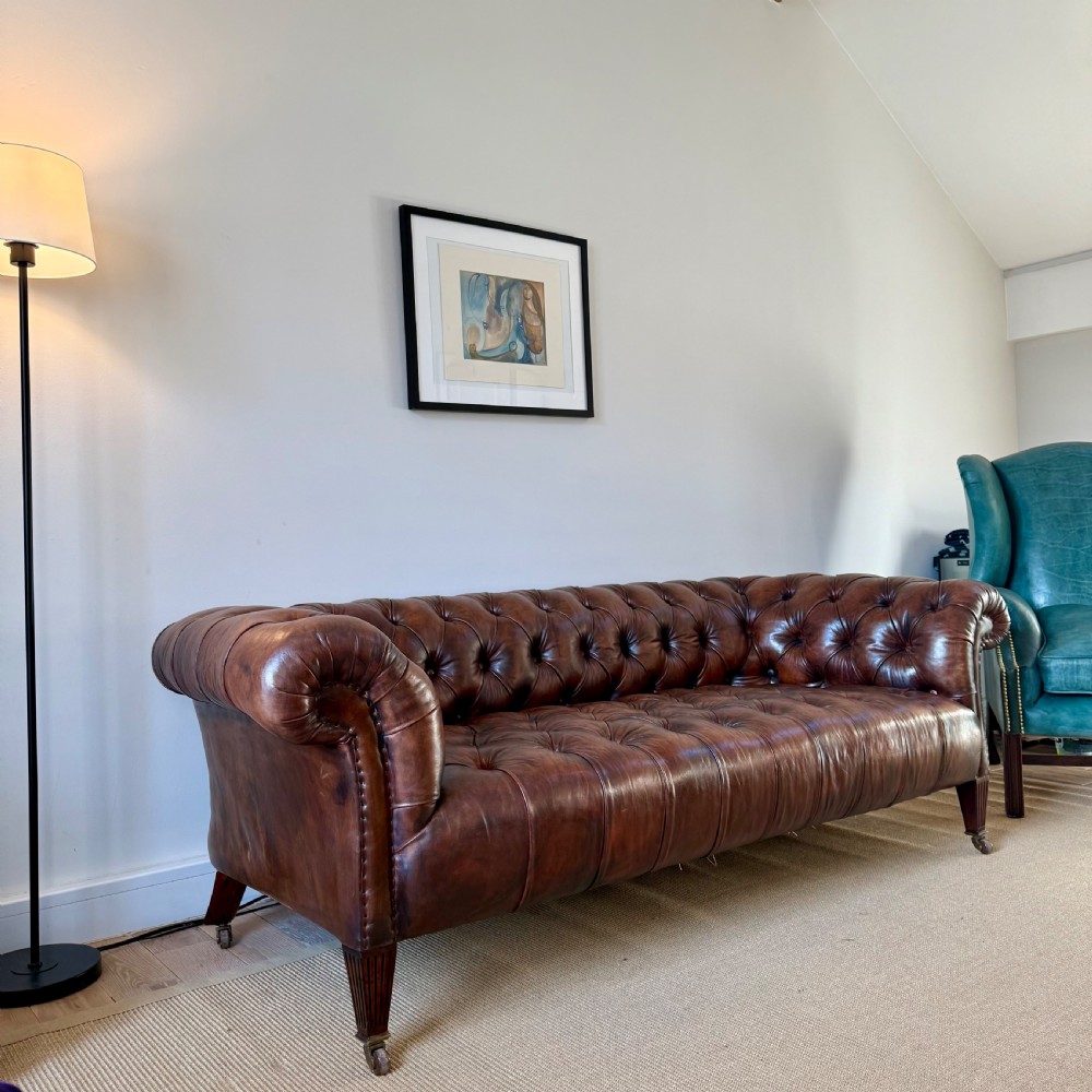 A 19th-century brown hand-dyed leather Chesterfield sofa featuring deep button tufting, rolled arms, and reeded wooden legs on brass castors. View III