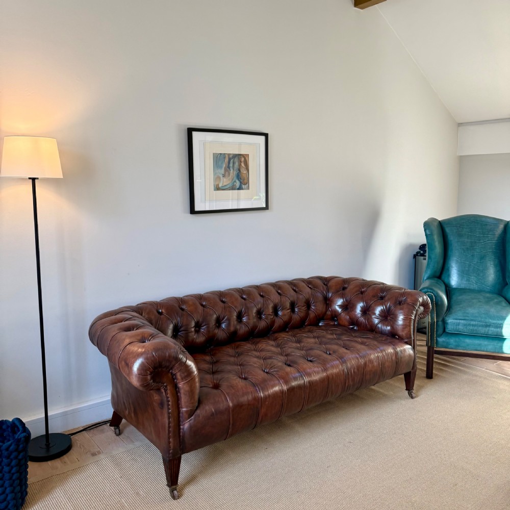 A 19th-century brown hand-dyed leather Chesterfield sofa featuring deep button tufting, rolled arms, and reeded wooden legs on brass castors. View IV