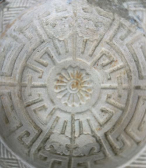 fig 2. A circular off-white antique ceramic dish featuring a scalloped rim, central meander pattern, and subtle marine mineral deposits.