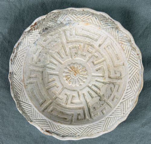 fig 4. A circular off-white antique ceramic dish featuring a scalloped rim, central meander pattern, and subtle marine mineral deposits.