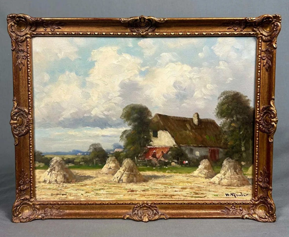 A framed oil painting depicting a rural harvest field with haystacks, a thatched farmhouse, and a cloudy sky set within an ornate gilded frame.