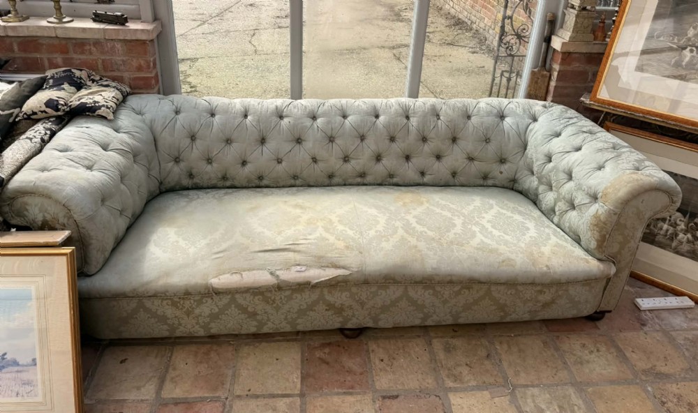 A large antique Chesterfield sofa featuring deep buttoned pale blue damask fabric upholstery, rolled arms, and turned wooden feet.