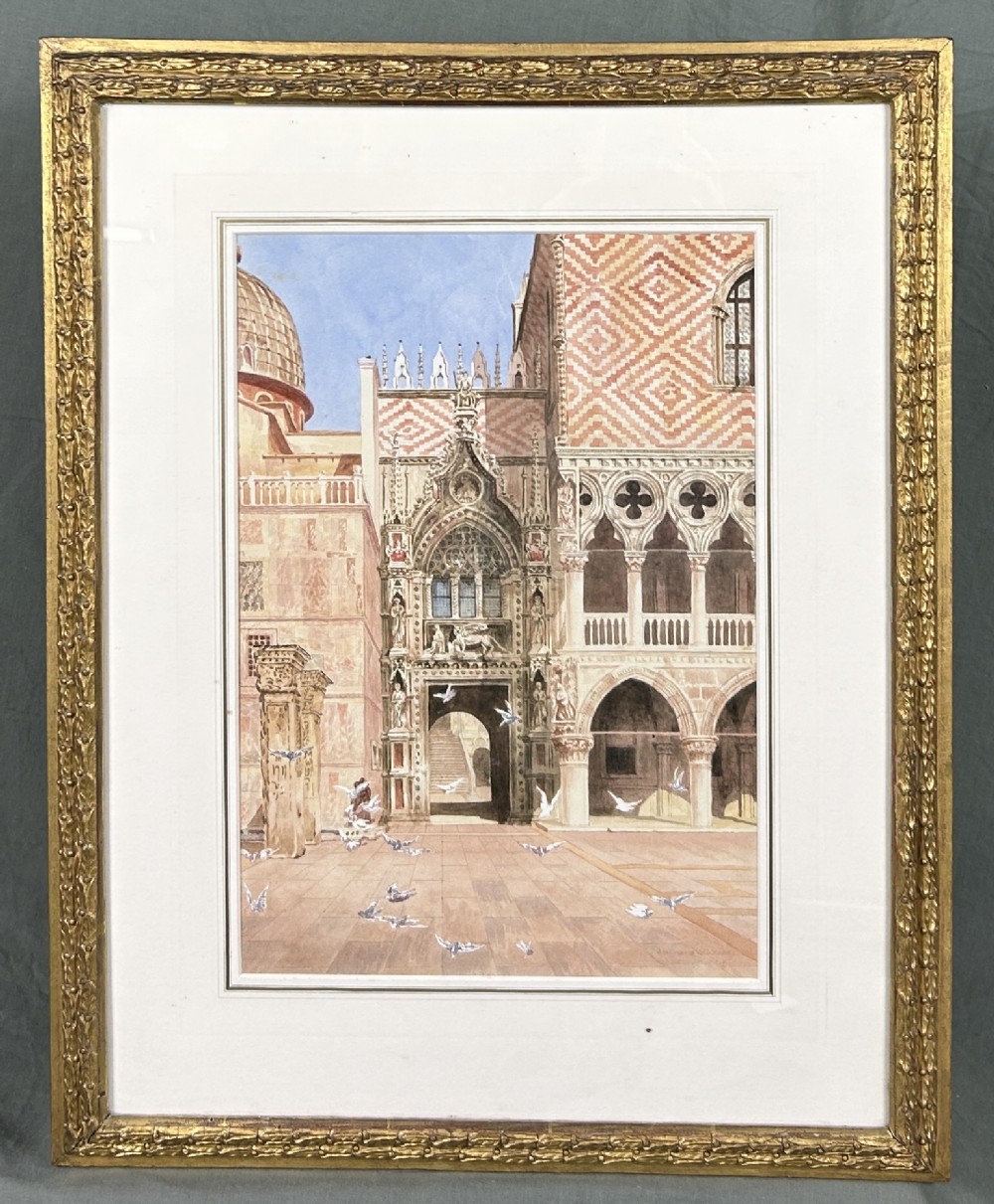 A framed watercolour painting portraying the detailed architectural facade of St Marks Square in Venice with flying pigeons, encased in an ornate gilded frame.