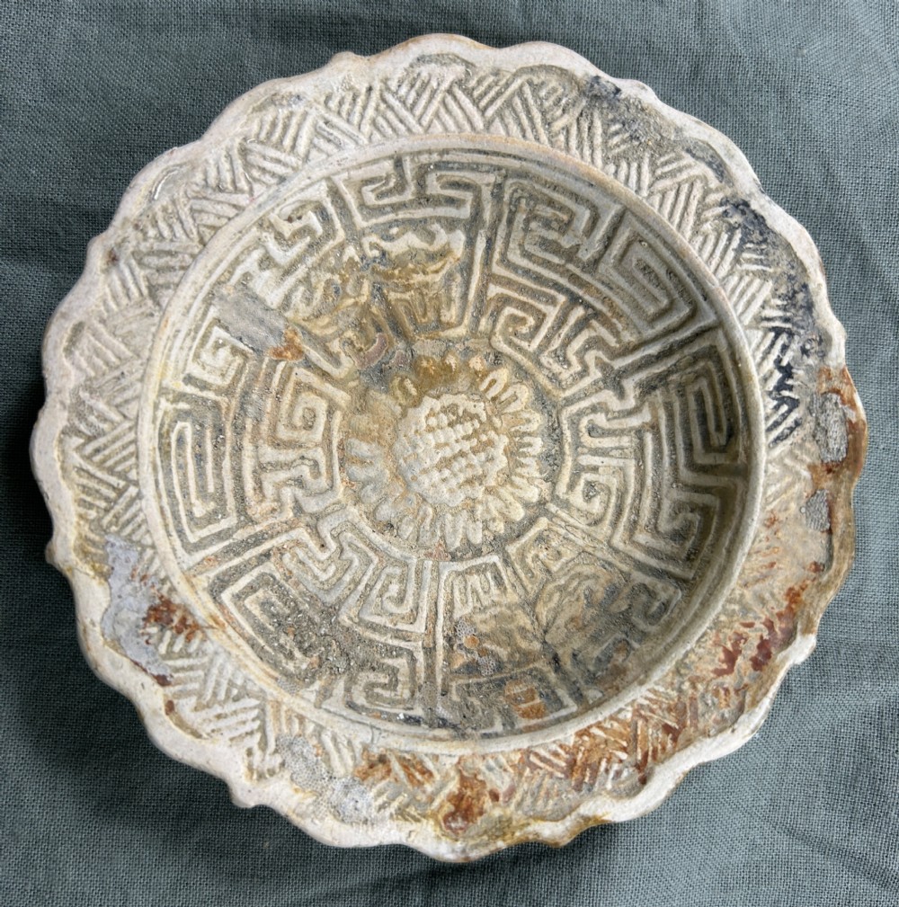 A circular off-white antique ceramic dish featuring a scalloped rim, central meander pattern, and subtle marine mineral deposits. View II