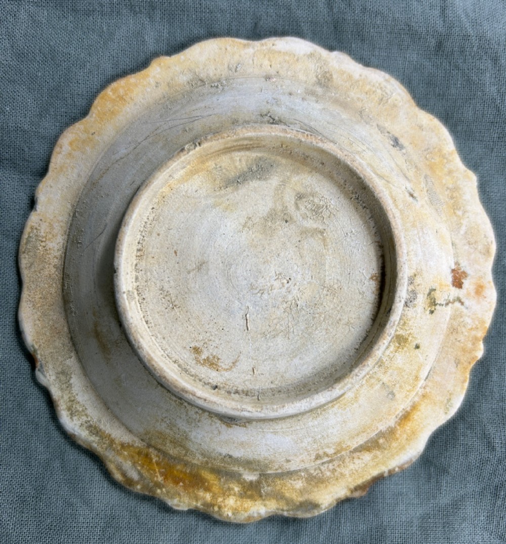 A circular off-white antique ceramic dish featuring a scalloped rim, central meander pattern, and subtle marine mineral deposits. View III
