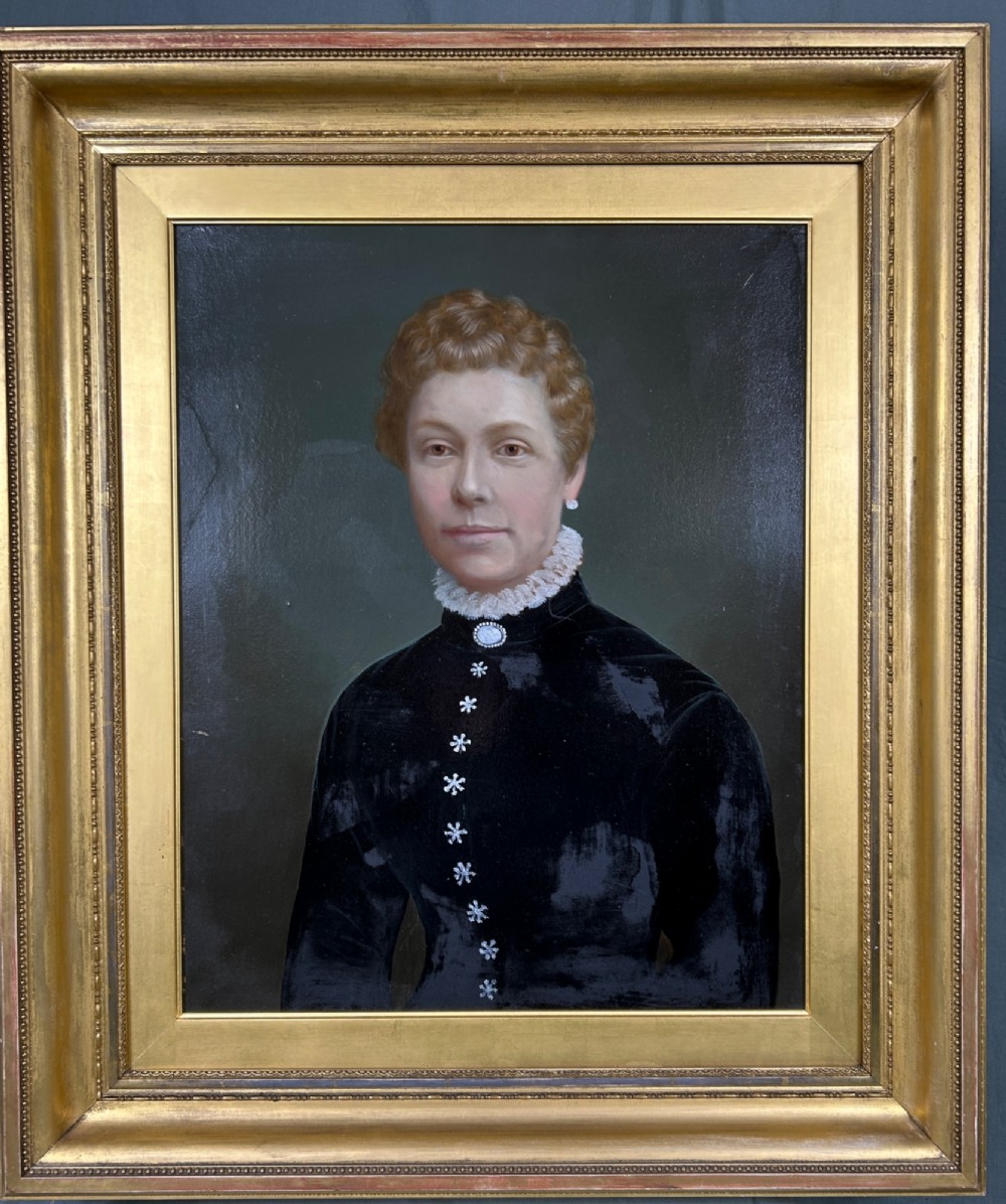 A 19th-century oil painting on board depicting a woman with auburn hair in a dark blue velvet dress with a white lace collar, presented in a gilded wooden frame.