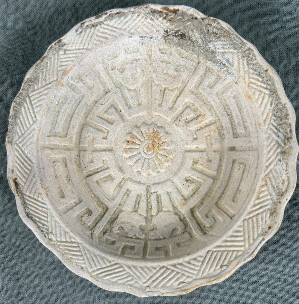 A circular off-white antique ceramic dish featuring a scalloped rim, central meander pattern, and subtle marine mineral deposits. View II