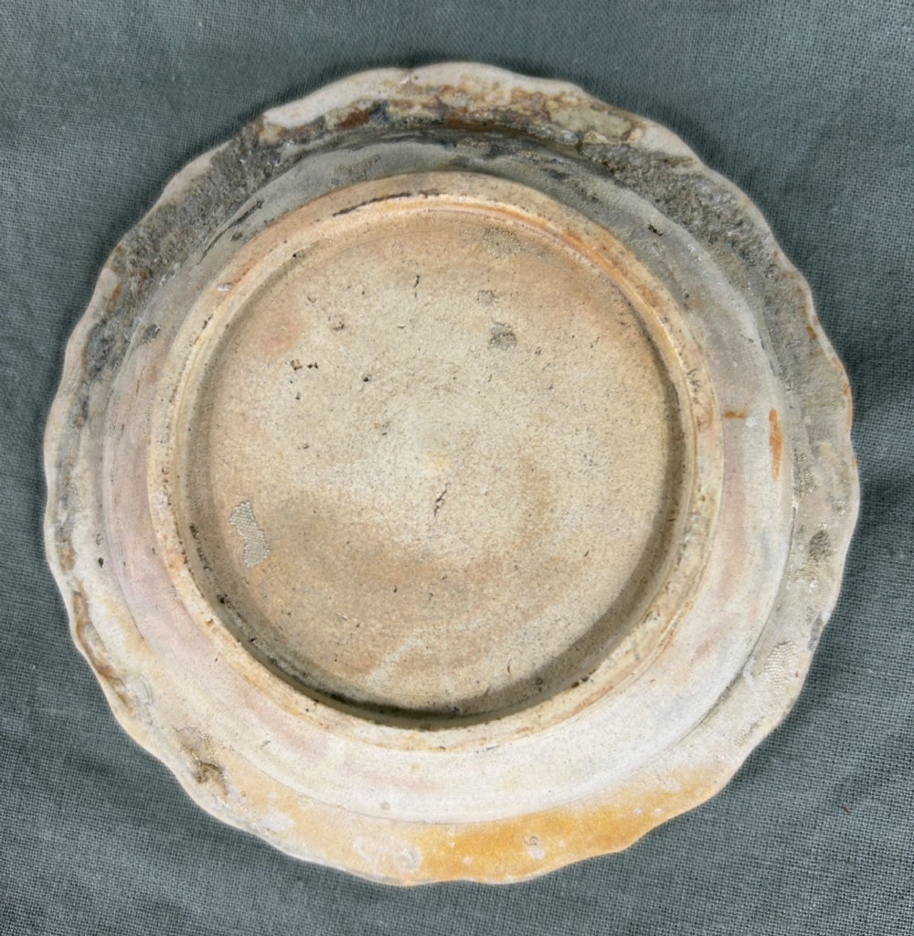 A circular off-white antique ceramic dish featuring a scalloped rim, central meander pattern, and subtle marine mineral deposits. View IV
