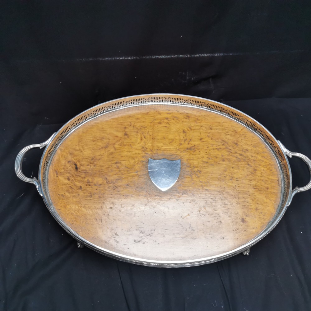 An oval antique oak serving tray with a silver-plated pierced gallery rim, twin handles, and an unengraved shield cartouche in the centre.