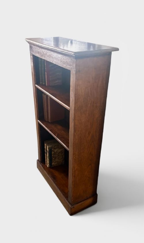 A narrow Edwardian oak open bookcase featuring adjustable wooden shelves and a simple plinth base. View IV