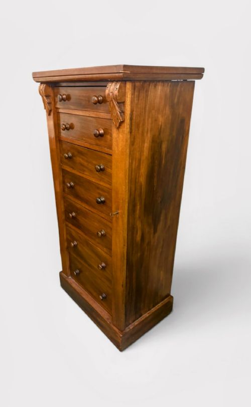 A tall Victorian walnut Wellington chest featuring seven stacked drawers, a right-hand locking stile, carved corner corbels, and turned wooden handles on a plinth base. View III