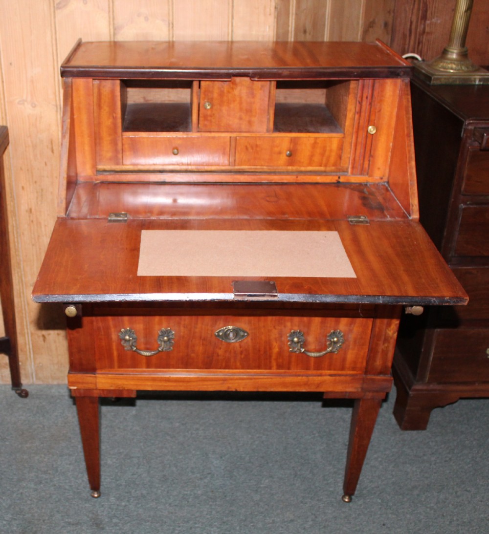 An Edwardian satinwood writing bureau featuring a sloping fall-front lid, two lower drawers with brass drop handles, dark crossbanded edging, and square tapered legs on castors. View V