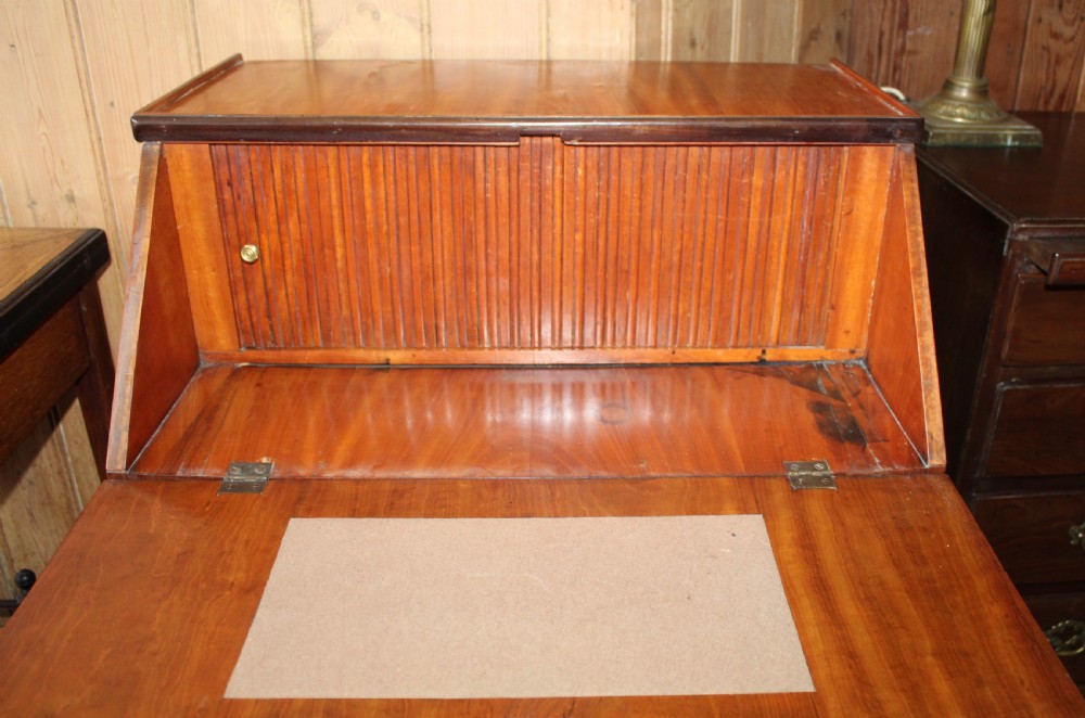 An Edwardian satinwood writing bureau featuring a sloping fall-front lid, two lower drawers with brass drop handles, dark crossbanded edging, and square tapered legs on castors. View VII