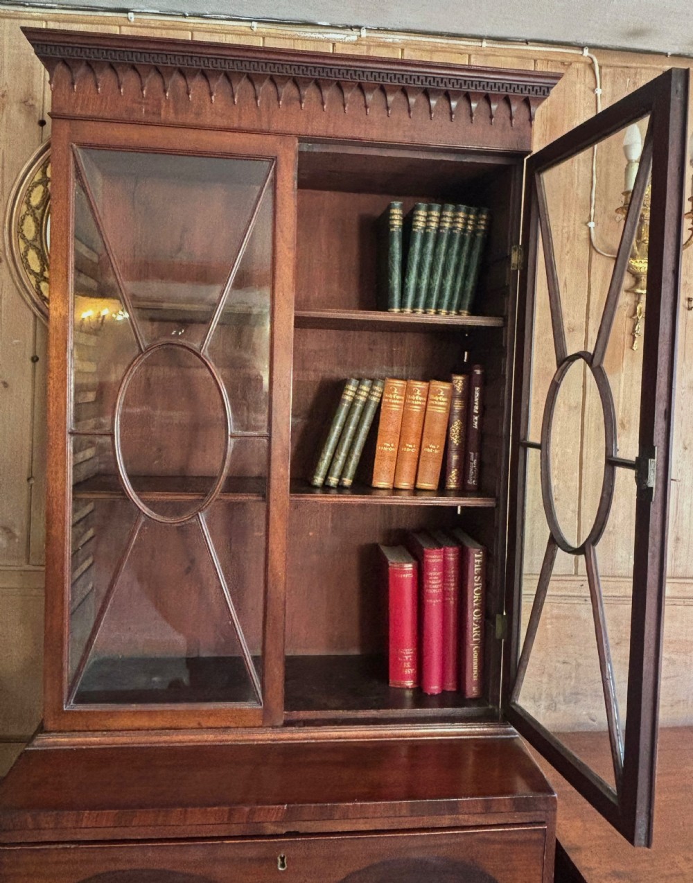 A Regency mahogany secretaire bookcase featuring glazed double doors with geometric astragal glazing above a chest of drawers with brass ring handles. View IX